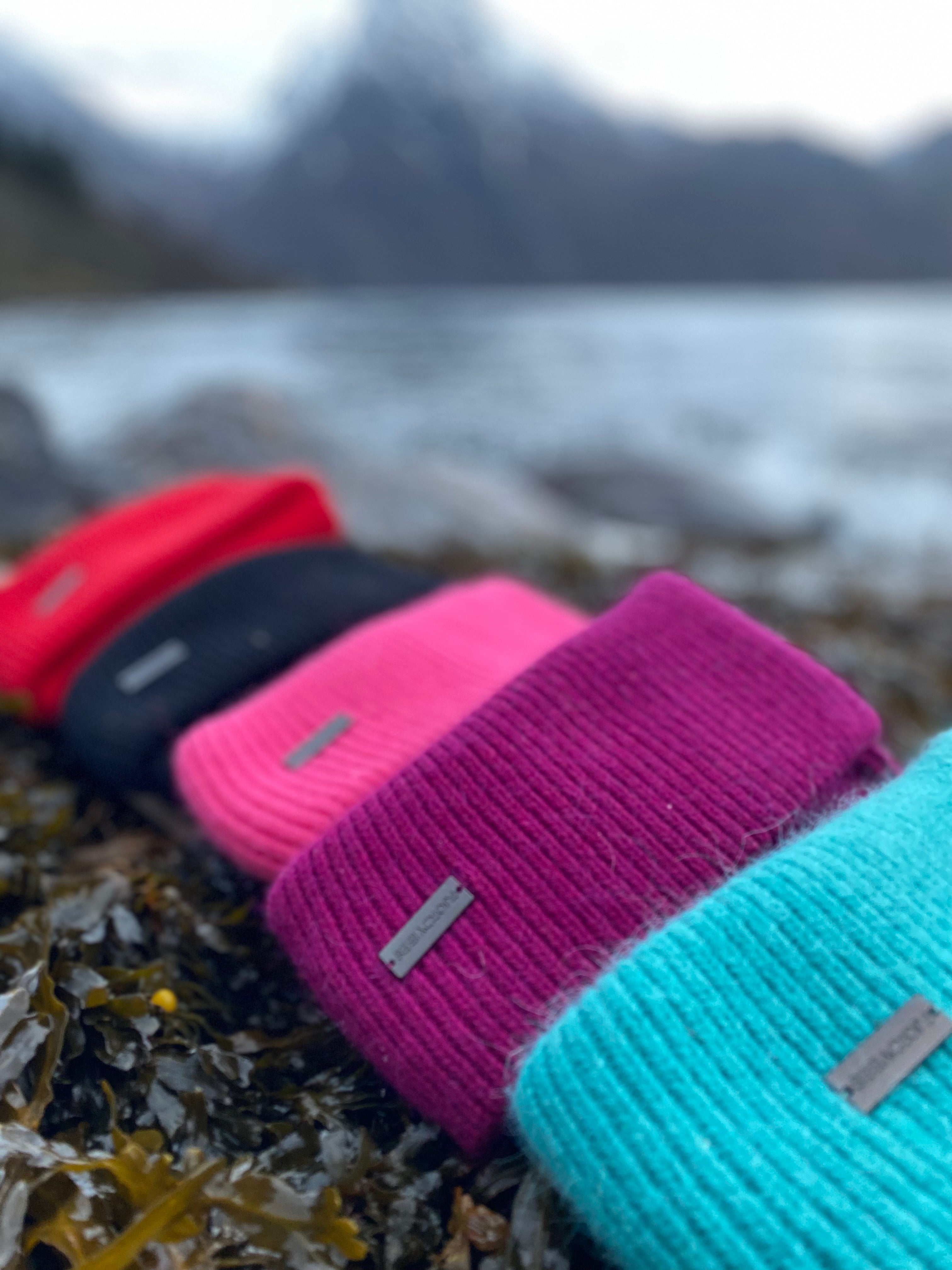 Fjord Vibes ull-luer ligger på rekke nede ved fjorden, i mange spreke farger