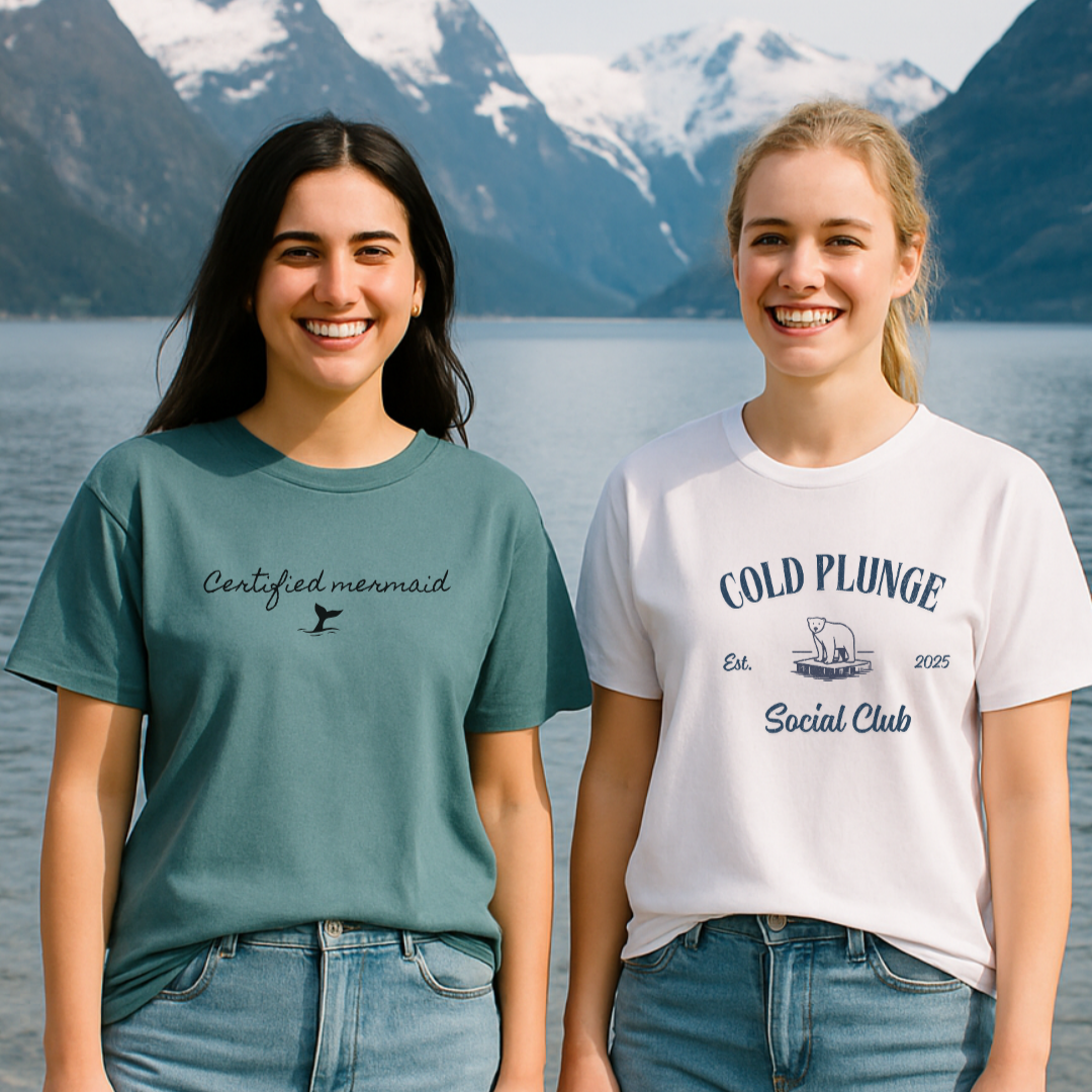 To damer som står i vannkanten ved en norsk fjord. De har på seg t-skjorter med is-bading motiv fra DoUdare