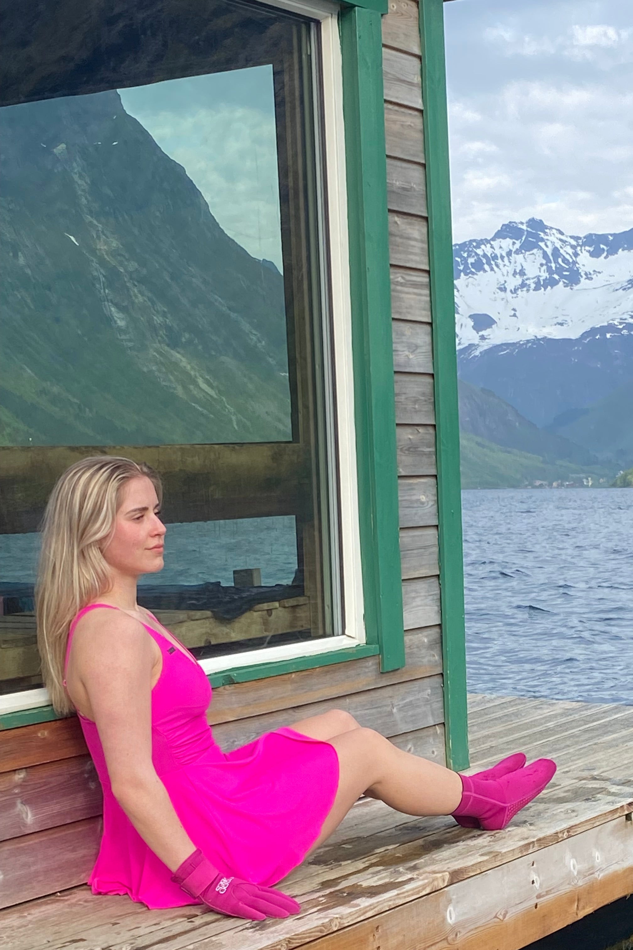 Ei dame som sitter utenfor en sauna, hun har på rosa badekjole og matchende rosa neopren-hansker og sokker