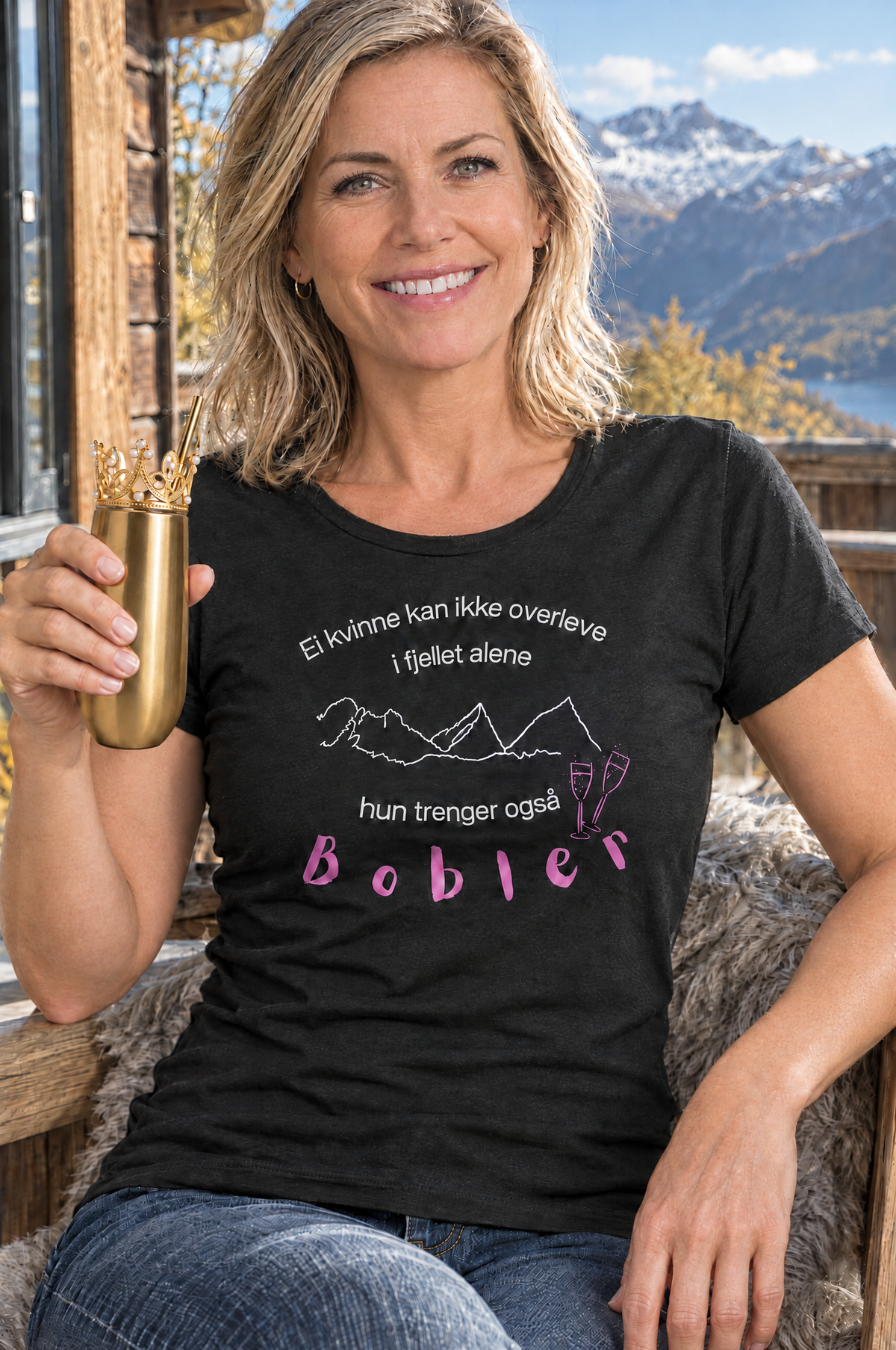 Dame på hytteterrasse i fjellet med svart prosecco t-skjorte med Til Fjells-trykk og proseccokopp i gull med prinsessekrone – Fjord Vibes